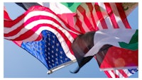 a group of flags flying in the air against a blue sky