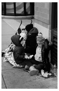 a black and white photo of a group of people sitting on the sidewalk