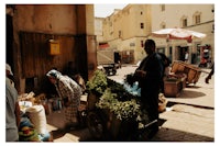 a man is selling vegetables on a cart in an alleyway