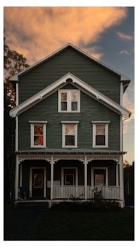 a green house with a white porch at sunset