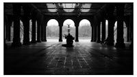 a black and white photo of a man sitting in an archway